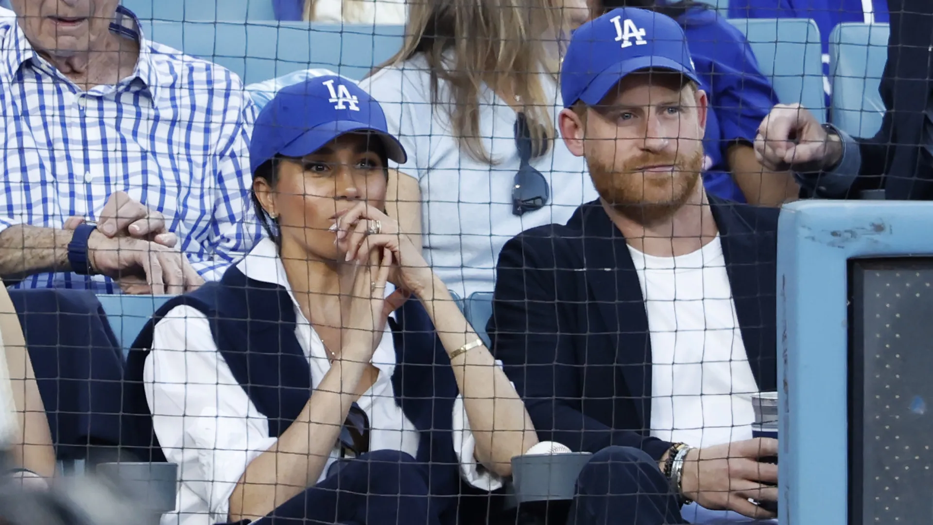 
                    Meghan Markle e o príncipe Harry nas bancadas de jogo de basebol
                