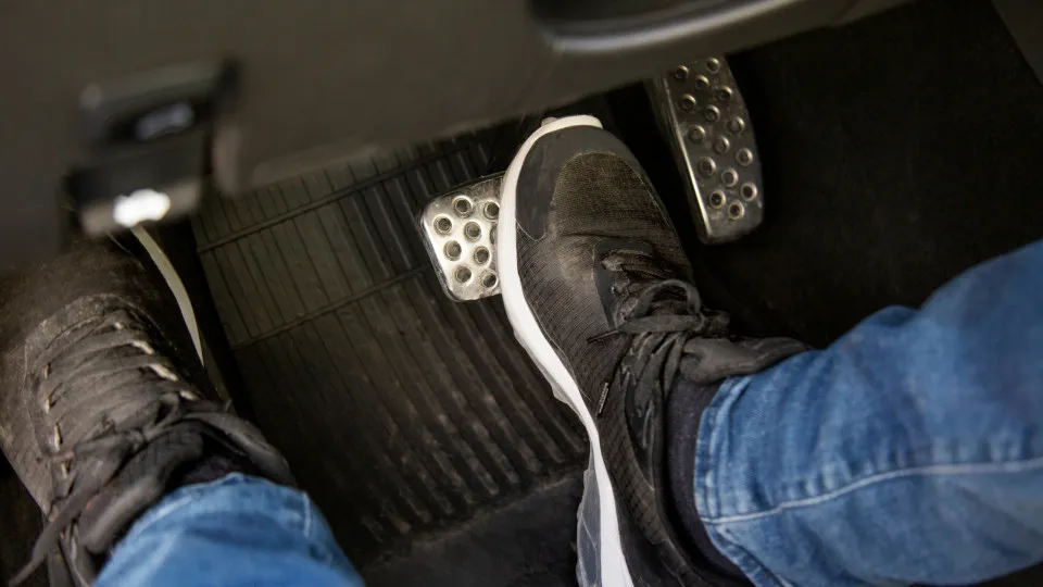 Condutor a ir travar, com o pedal de embraiagem acionado.